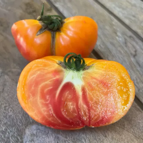 Orangeröd tomat av sorten Ananas liggandes på bord hel och i halvor.